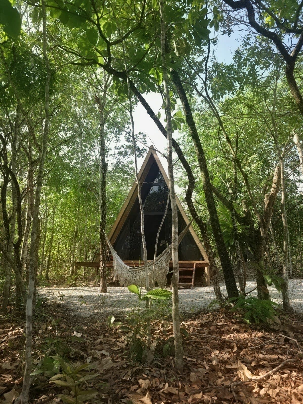 Chalé triangular entre as árvores do cerrado, com rede em frente