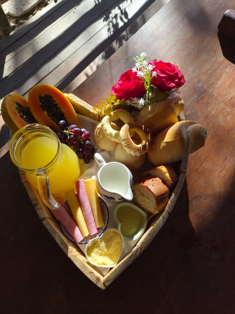 Bandeja em forma de coração com frutas, pães, frios, suco e rosas vermelhas