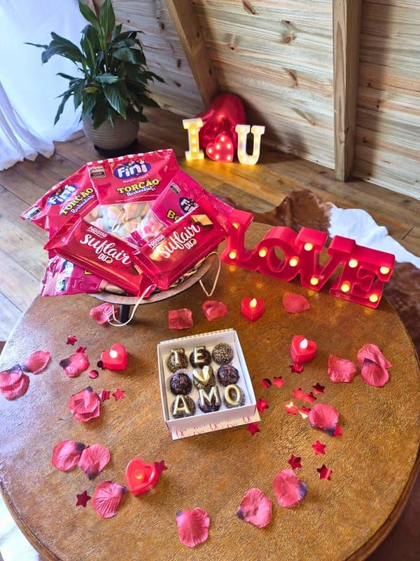 Mesa com letreiro LOVE, chocolates, pétalas de rosa e velas