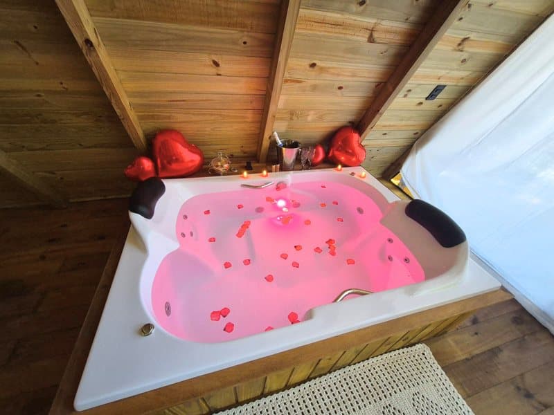 Banheira de hidromassagem com luz rosa, pétalas e balões de coração