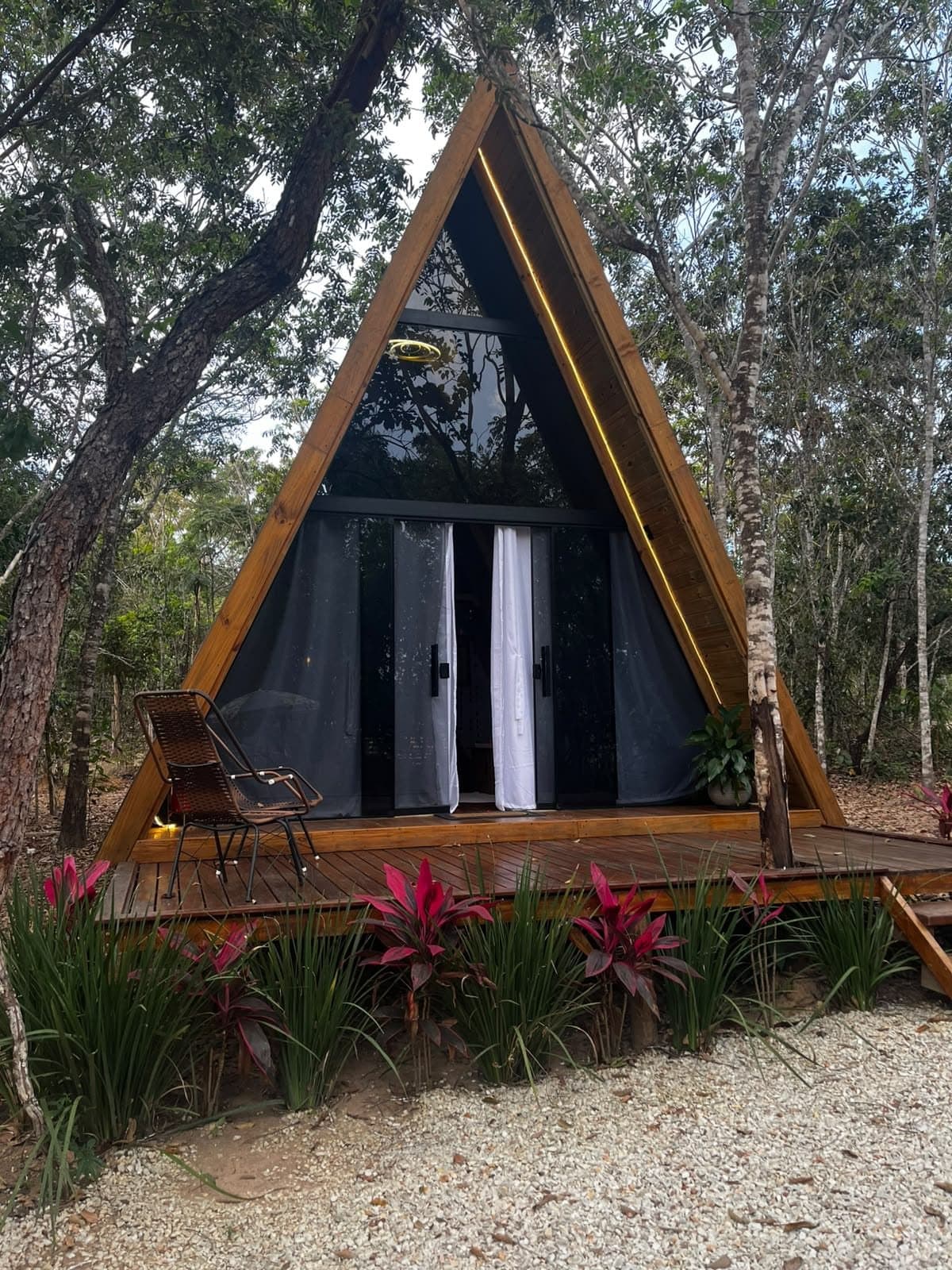 Fachada triangular do Chalé Tulipa, com deck de madeira e canteiro de flores vermelhas entre as árvores